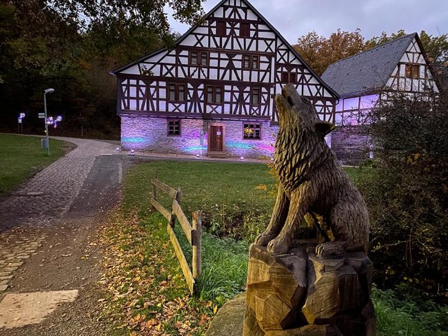 Holzfigur eines Wolfes vor illuminiertem Fachwerkhaus im Freilichtmuseum