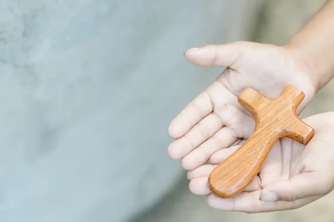 Hände, die ein Kreuz halten. Foto: Adobe Stock.