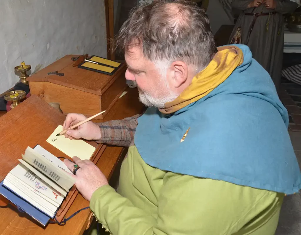 Mann in historischer Kleidung beim Abschreiben eines Buches.