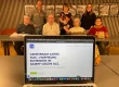 Laptopbildschirm zeigt Internetseite der Gernot-Bohn-ALS-Stiftung, dahinter Mitglieder des Vereins.