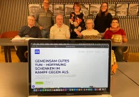 Laptopbildschirm zeigt Internetseite der Gernot-Bohn-ALS-Stiftung, dahinter Mitglieder des Vereins.